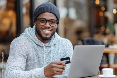 Young man smiles while holding a credit card in a cozy cafe setting during th...