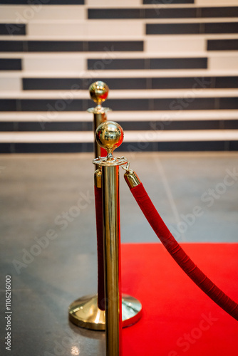 There exists a luxurious goldcolored pole holding up a vibrant red rope that stretches between it, along with an elegant red carpet laid out beneath it, creating a striking visual contrast photo