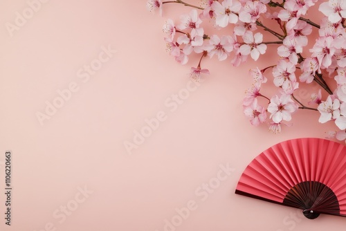 Cherry blossom branches and a red fan create a serene composition on a soft b...