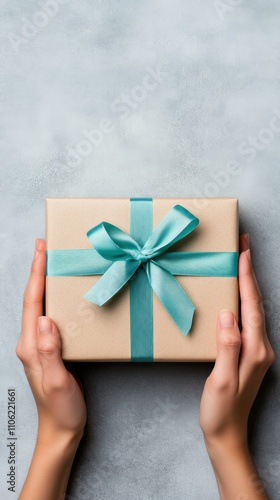 Gift wrapped in elegant paper with a blue ribbon held by hands against a fest...