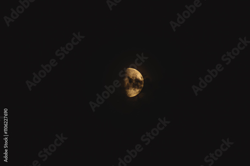 a large crescent moon illuminated against a stark, dark night sky. The surface of the moon is visible with various textures and craters, creating a detailed appearance. photo