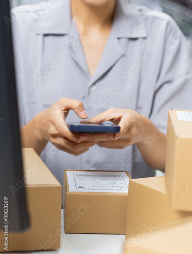 Asian female small business shop owner using application on smartphone scanning QR code on parcel box for checking shipment information and order number to prepare for delivery at warehouse office.