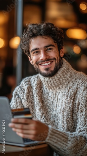 Smiling young man working on laptop in cozy cafe with credit card in hand