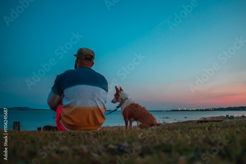 Hombre con su perra podenco pequeño observando una puesta de sol en el mar, creando una escena relajante de conexión y naturaleza. photo