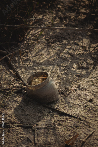 a weathered glass pot resting on a sandy surface. The pot is slightly tilted, revealing its round base and narrow opening photo