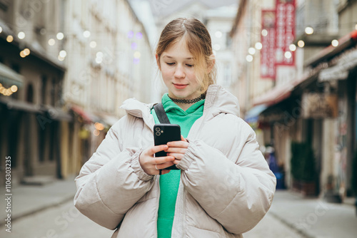 Stylish teenage girl uses a smartphone while walking along a city street. photo