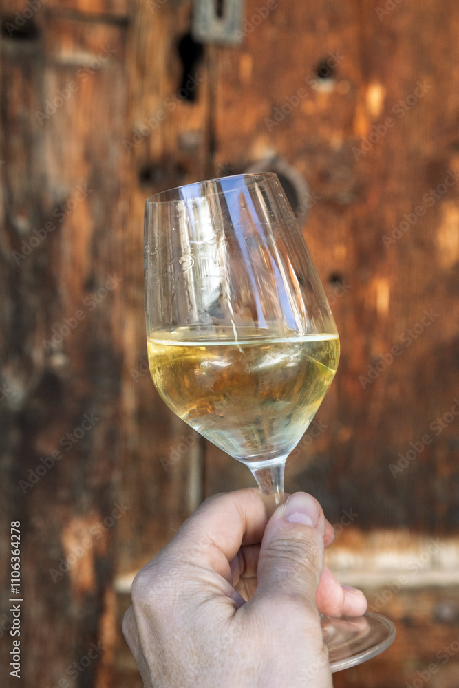 Obraz premium Verre de vin blanc tenu à la main devant une porte de vieux bois
