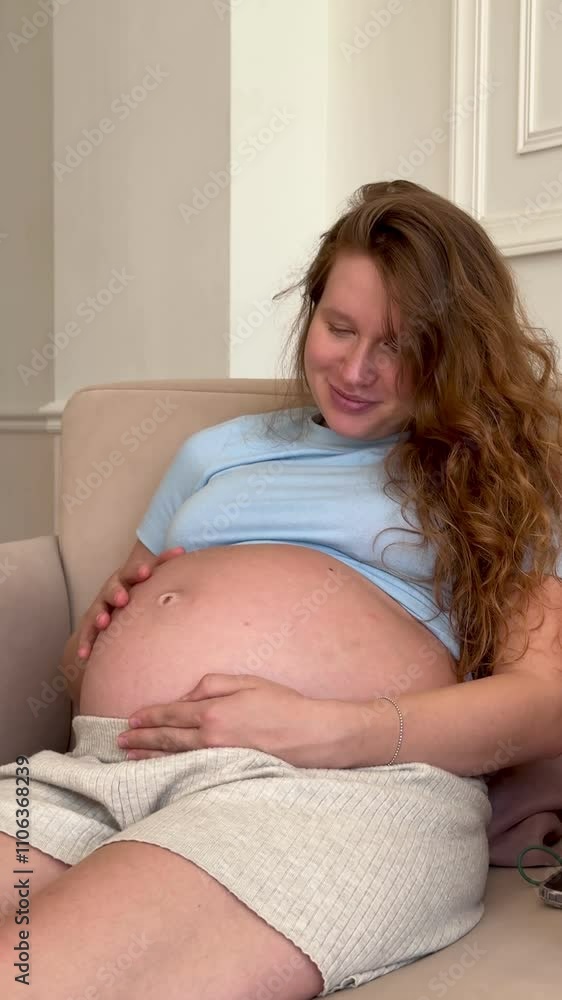 Young pregnant happy woman stroking her belly at home in living room Young pregnant happy woman stroking her belly at home in living room
