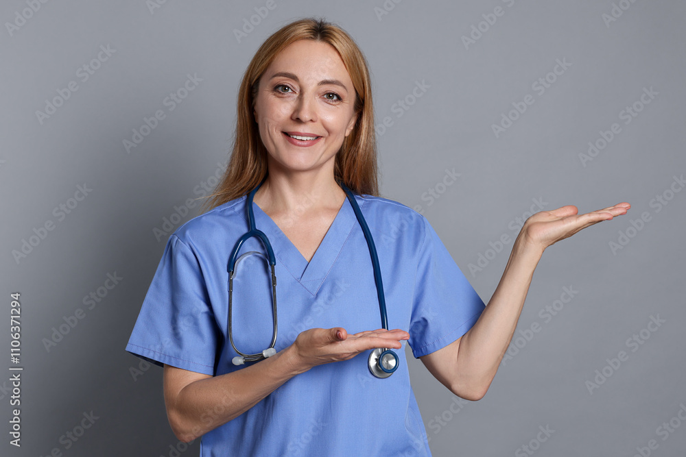 Doctor with stethoscope showing something on gray background Doctor with stethoscope showing something on gray background