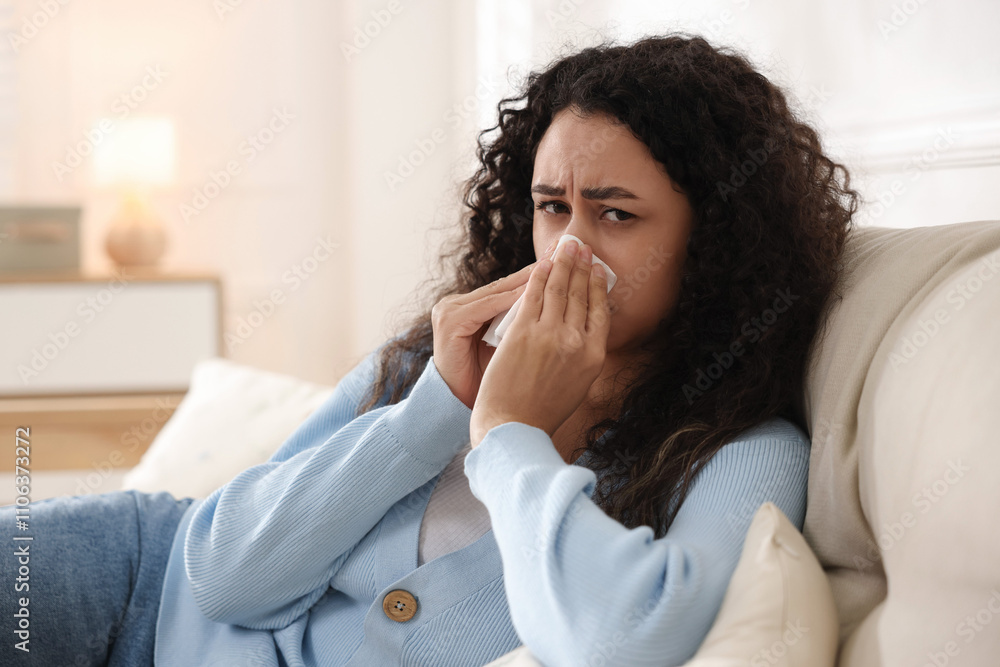 Young woman with tissue blowing runny nose at home Young woman with tissue blowing runny nose at home
