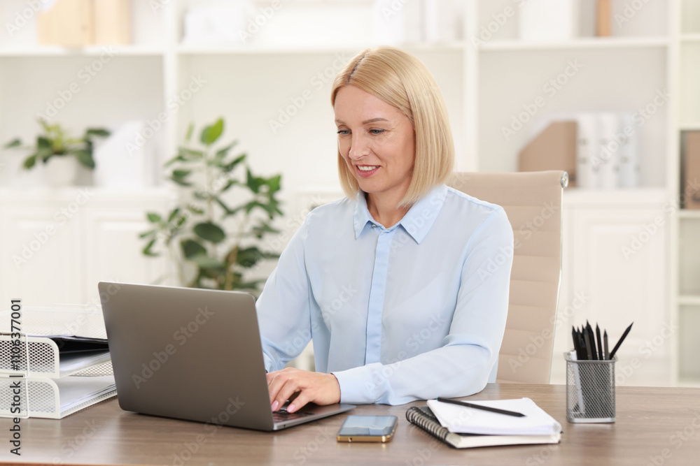 Smiling middle aged woman working with laptop at table in office Smiling middle aged woman working with laptop at table in office