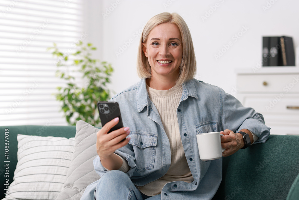 Smiling middle aged woman with cup of hot drink using smartphone at home Smiling middle aged woman with cup of hot drink using smartphone at home