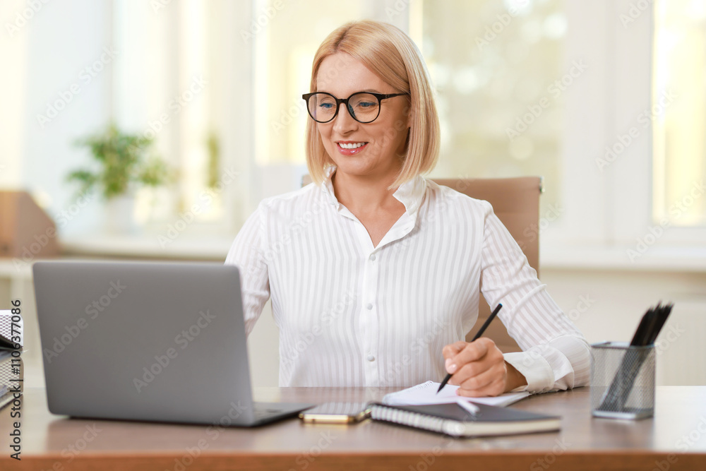 Smiling middle aged woman working with laptop at table in office Smiling middle aged woman working with laptop at table in office