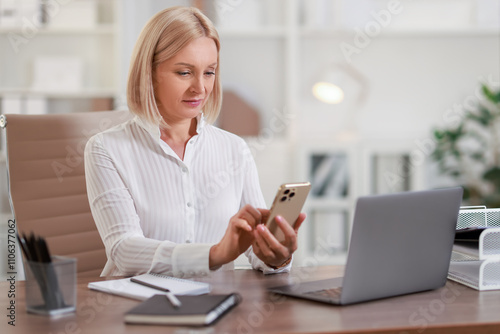 Middle aged woman using smartphone at table in office