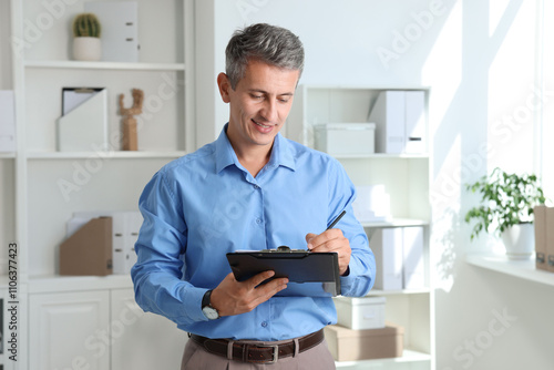 Smiling middle aged man writing on clipboard in office