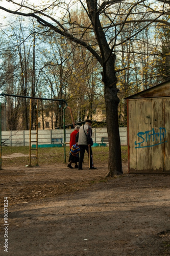 Wallpaper Mural A couple walks hand-in-hand through a quiet park past a rusty playground. Tall trees stand bare, and a shed is painted with the word "STAY." The scene captures a peaceful, nostalgic atmosphere. Torontodigital.ca