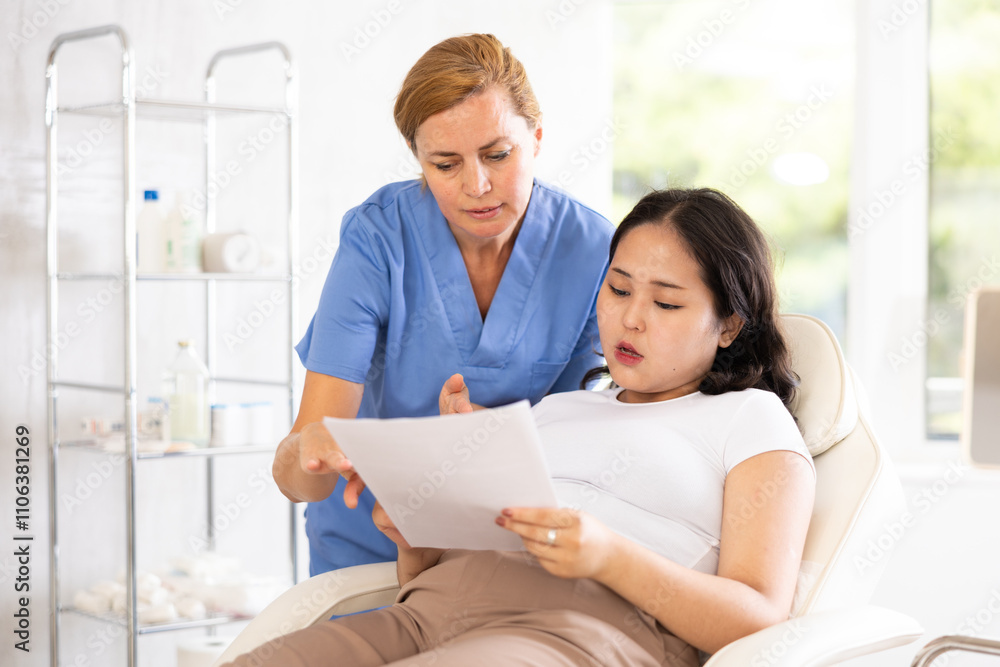 Portrait of middle-aged doctor consulting young asian woman in hospital with help of documents Portrait of middle-aged doctor consulting young asian woman in hospital with help of documents
