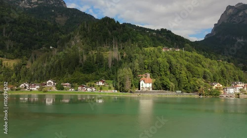 Wallpaper Mural Slow-motion drone footage captures alpine houses along Lago di Alleghe, with lush forested hills and Dolomite peaks in the background. The peaceful lakeside setting showcases Italian natural beauty. Torontodigital.ca