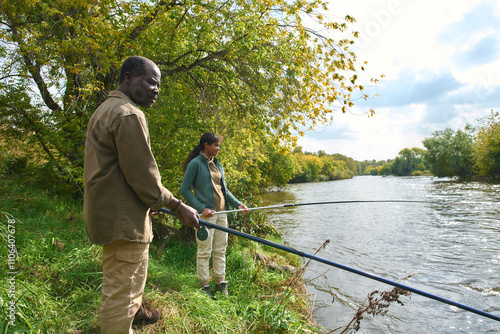 African American father and daughter spending spare time under open sky together while they fishing