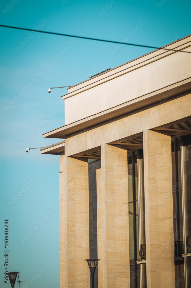 a modern building with a sleek stone facade, complemented by strong, angular columns. A clear blue sky serves as the backdrop, enhancing the architectural details a modern building with a sleek stone facade, complemented by strong, angular columns. A clear blue sky serves as the backdrop, enhancing the architectural details