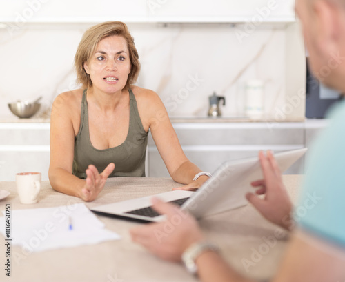 Middle-aged woman agent communicating kindly with male business-partner sitting at the kitchen-table photo