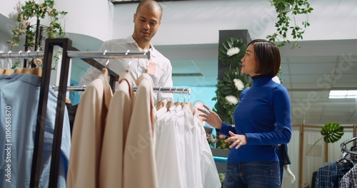 Middle eastern shop employee assisting asian woman in choosing the right size for clothes, ensuring a great consumer behavior and shopping experience. Presenting clothing options. Camera B. photo