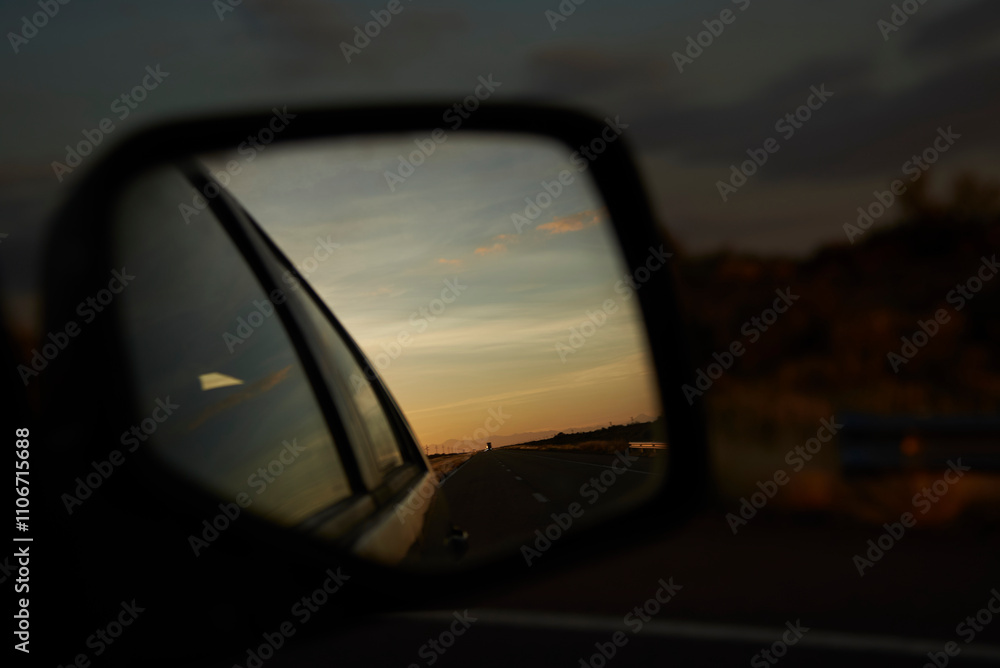 Rear view mirror of a traveling vehicle, in the reflection you can see the road at sunset. Concept: returning home after a car trip. Rear view mirror of a traveling vehicle, in the reflection you can see the road at sunset. Concept: returning home after a car trip.