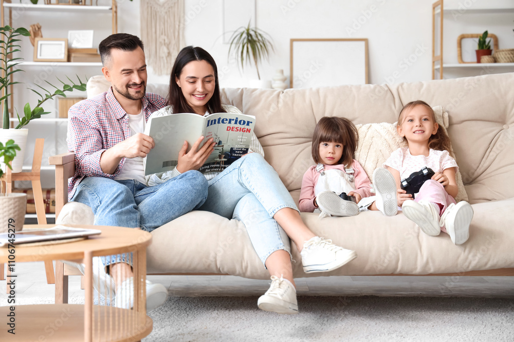Happy sisters playing video games while their parents reading magazine on sofa at home Happy sisters playing video games while their parents reading magazine on sofa at home