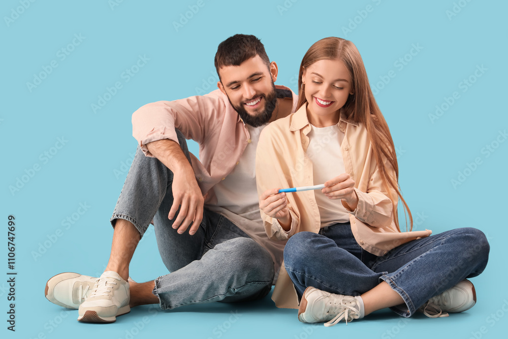 Happy young couple with pregnancy test sitting on blue background Happy young couple with pregnancy test sitting on blue background