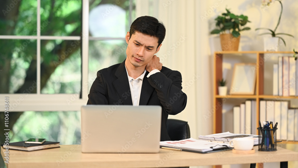 Exhausted businessman having neck ache while working at his desk in the office Exhausted businessman having neck ache while working at his desk in the office