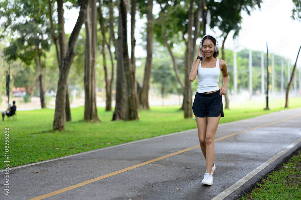 Sporty young woman with headphones jogging along a park path Sporty young woman with headphones jogging along a park path