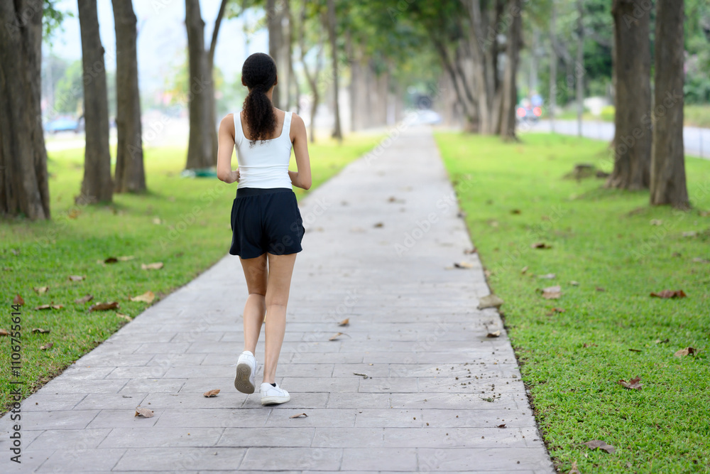 Young sportswoman jogging on a paved path through a park Young sportswoman jogging on a paved path through a park