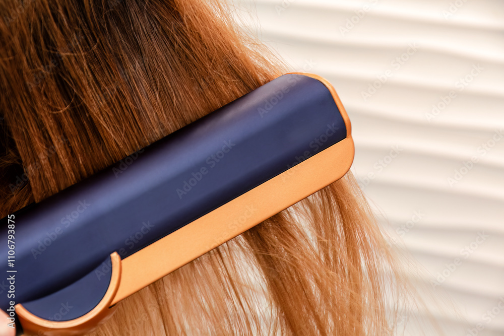 Fototapeta premium Close-up shot of a hair straightener gliding through long, light brown hair. Beauty fashion and styling tools