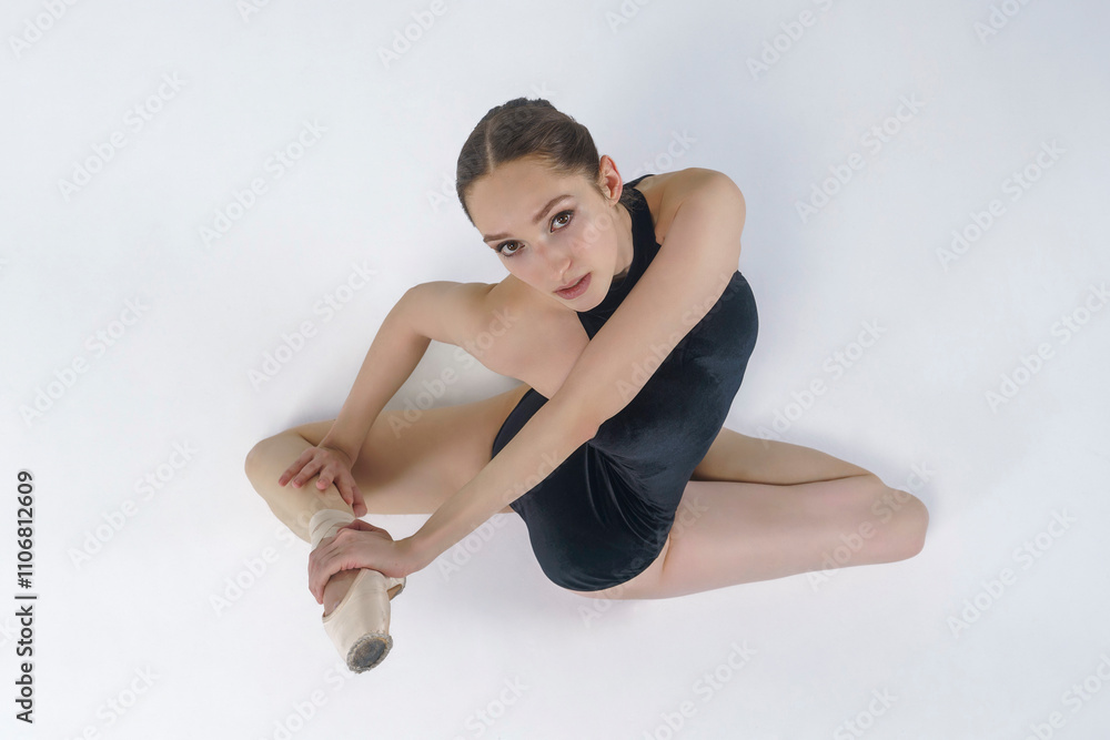 young ballerina in a dark bodysuit sitting on the floor shows stretching and eversion of her arms young ballerina in a dark bodysuit sitting on the floor shows stretching and eversion of her arms