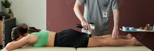 Woman lying prone on massage table while receiving therapeutic massage from male therapist wearing uniform in modern clinic setting