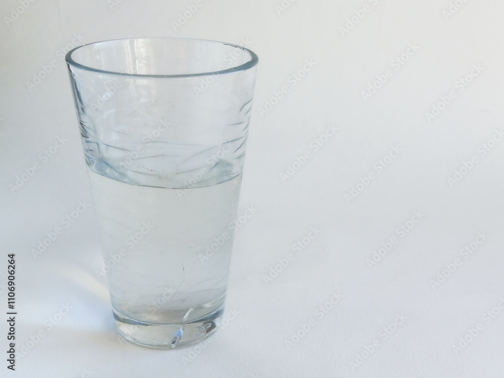 A transparent glass glass of water stands on the table, on a white background. Maintaining the body's water balance. Clean filtered water. A transparent glass glass of water stands on the table, on a white background. Maintaining the body's water balance. Clean filtered water.