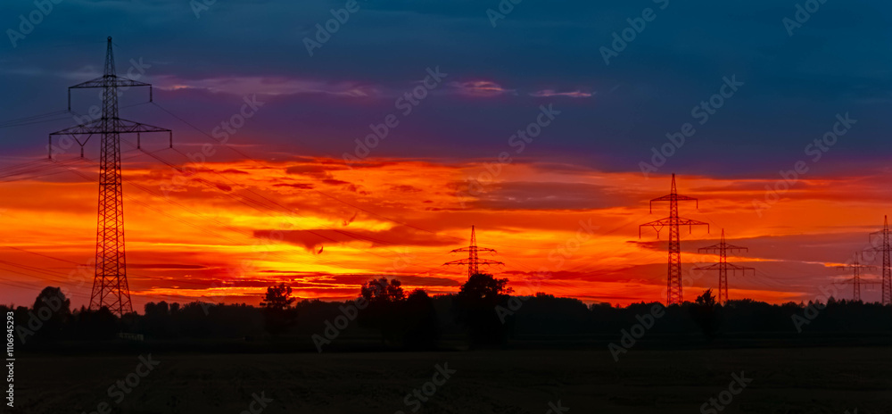 Fototapeta premium Summer sunset with a dramatic sky and overland high voltage lines near Tabertshausen, Deggendorf, Bavaria, Germany