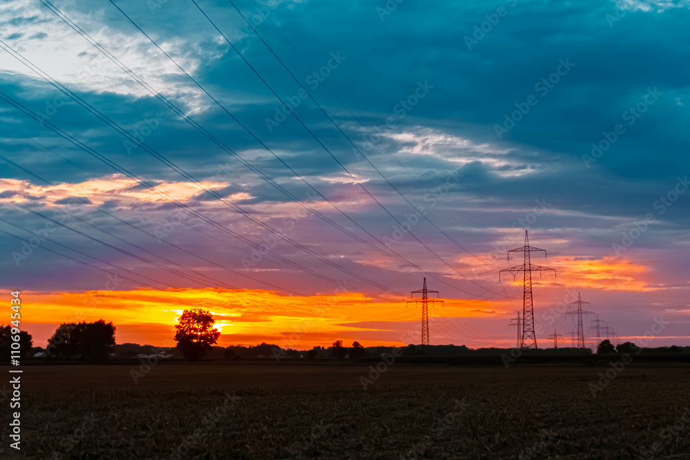 Fototapeta premium Summer sunset with a dramatic sky and overland high voltage lines near Tabertshausen, Deggendorf, Bavaria, Germany