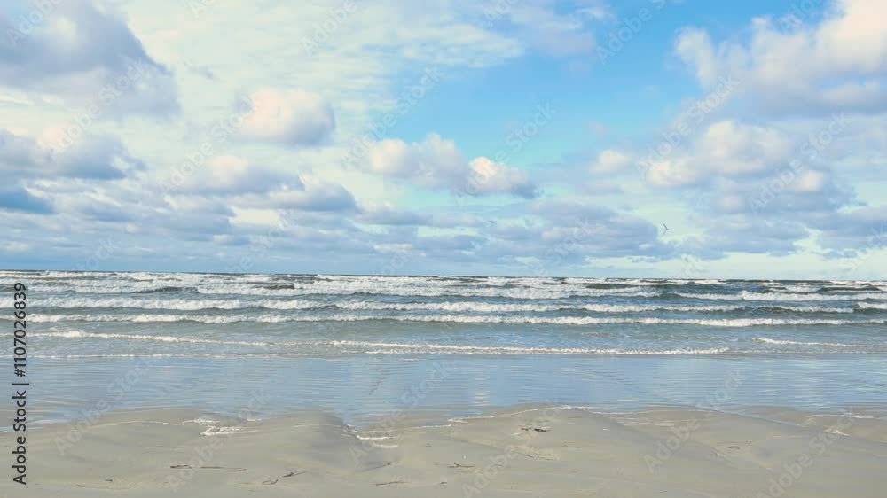 White foamy and bubbly ocean sea water waves moving to a sandy shoreline in slow motion during a windy and stormy day in Vääna Estonia while white clouds are in blue sky. Water is green and blue. White foamy and bubbly ocean sea water waves moving to a sandy shoreline in slow motion during a windy and stormy day in Vääna Estonia while white clouds are in blue sky. Water is green and blue.