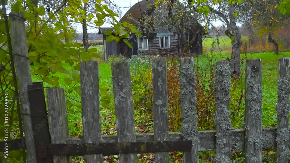 Old wooden and spooky house in a garden during a cloudy day in Saku Estonia during autumn time with green mowed grass surrounding it and yellow fallen leaves on trees. Mossy wooden fence in foreground Old wooden and spooky house in a garden during a cloudy day in Saku Estonia during autumn time with green mowed grass surrounding it and yellow fallen leaves on trees. Mossy wooden fence in foreground
