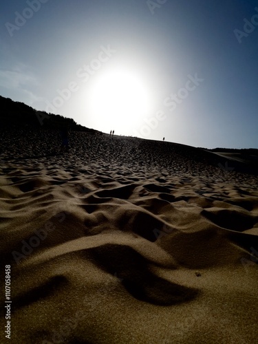 Vista horizontal de una duna de arena a ras del suelo, al fondo una siluetas humanas en la cima, tocando los rayos del sol, deslumbrados, ruta peregrinación  photo