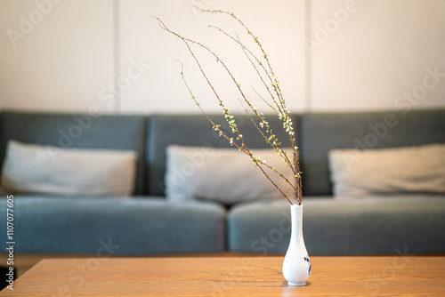 A Japanese style ceramic vase with cultivate hosueplant inside, it place on wooden desk in living room with sofa seat as blackground. Interior decoration object, close-up and selective focus. photo