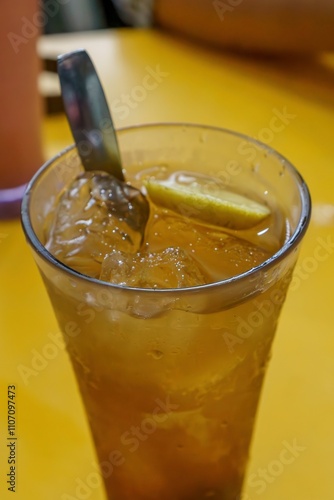 A refreshing glass of iced lemon tea with a lemon wedge, garnished with a sprig of mint, served with a spoon