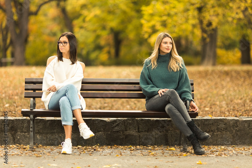 Two beautilful young women sitting on the bench in publiic park photo