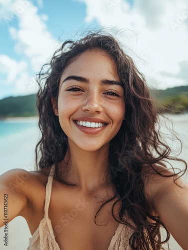 Portrait of smiling young woman taking a selfie at beach during. Cheerful hispanic woman enjoying at beach during holiday. Happy girl taking photo over exotic tropical beach looking at camera.