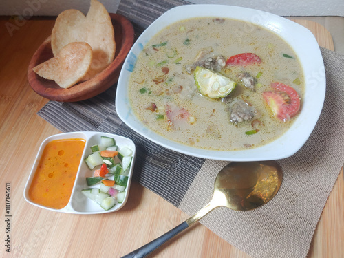 Soto Betawi on the wooden background, served with acar, chili sauce and shrimp crackers. Soto betawi is traditional food from betawi, indonesia. meat with milk soup and vegetable. savory taste photo