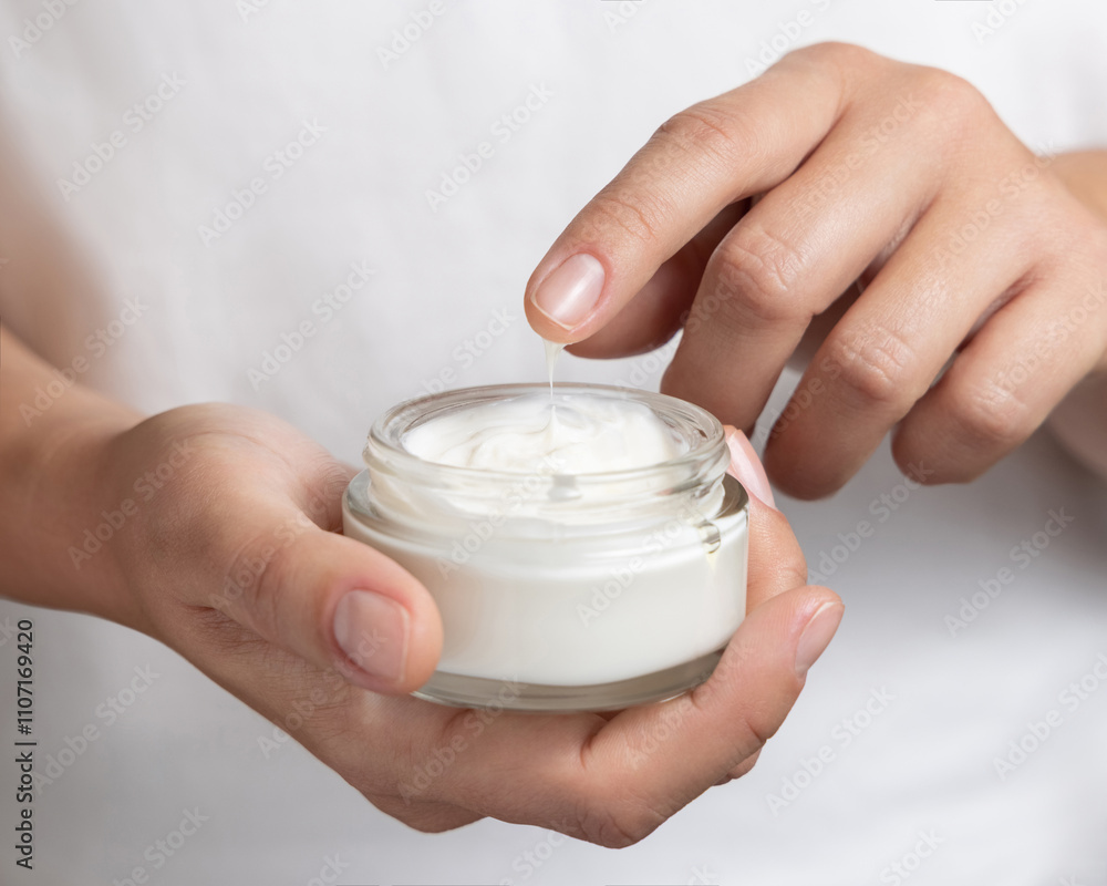 Woman touching cream with finger and holding a glass cosmetic jar in other hand, closeup Woman touching cream with finger and holding a glass cosmetic jar in other hand, closeup