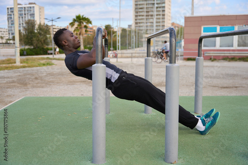 Young black man performing calisthenics on parallel bars in urban setting photo