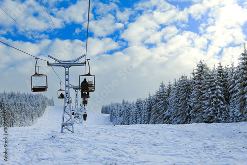 Skiers and snowboarders go up on chair-lift, snowy off-piste ski slope and high mountains. Sunny winter day. Carpathian mountains.