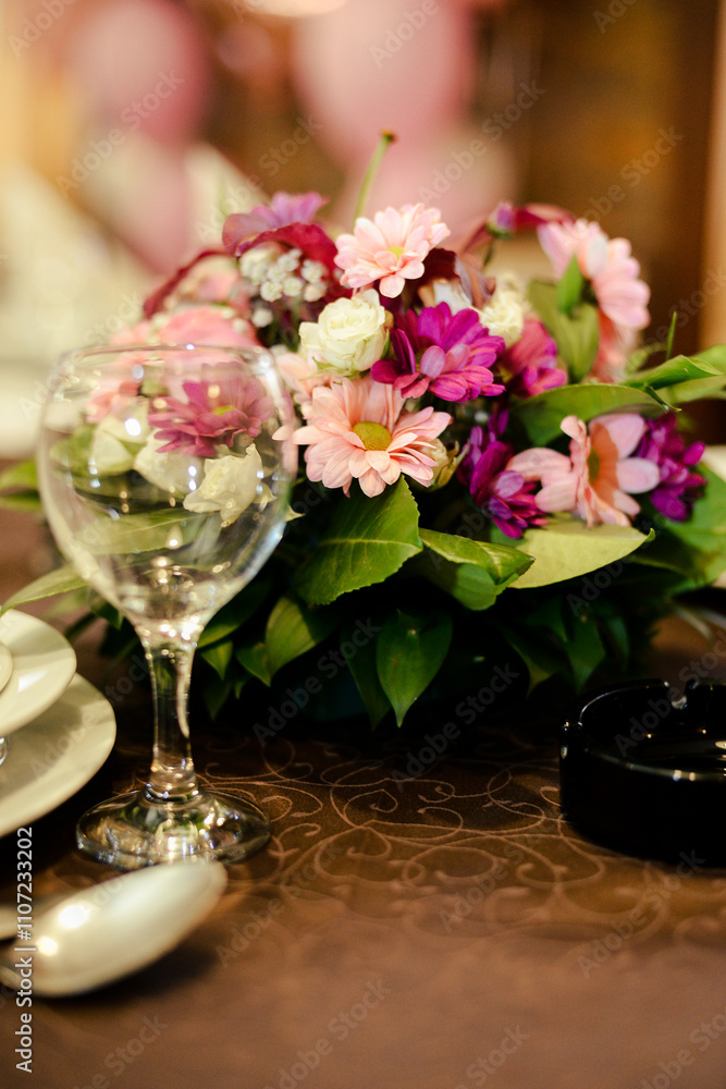 An empty wine glass on a served table next to which there is a bouquet of flowers as a decoration An empty wine glass on a served table next to which there is a bouquet of flowers as a decoration